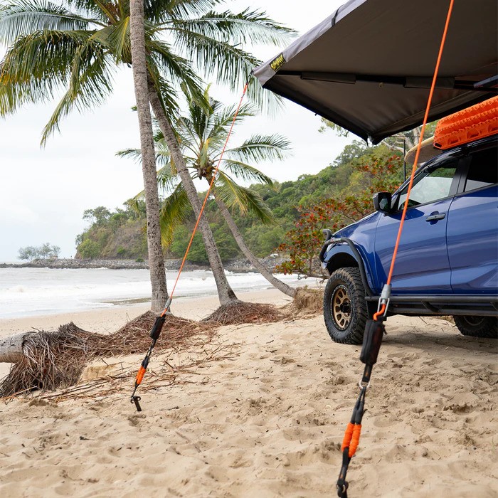 A truck is parked on a beach with its awning deployed.