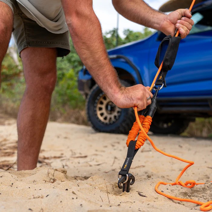 A guy rope is tightened on a beach.