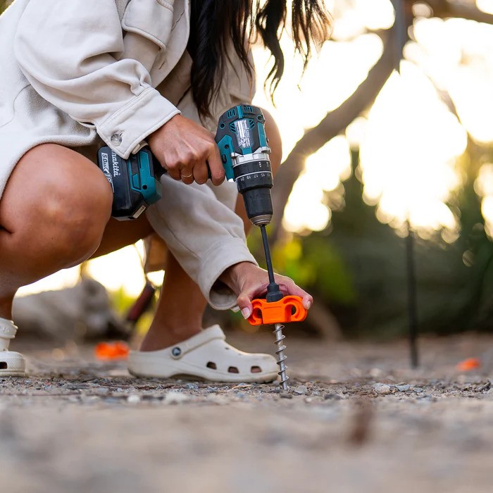 A woman uses a drill and a Tiegear hard terra peg to secure her awning. 