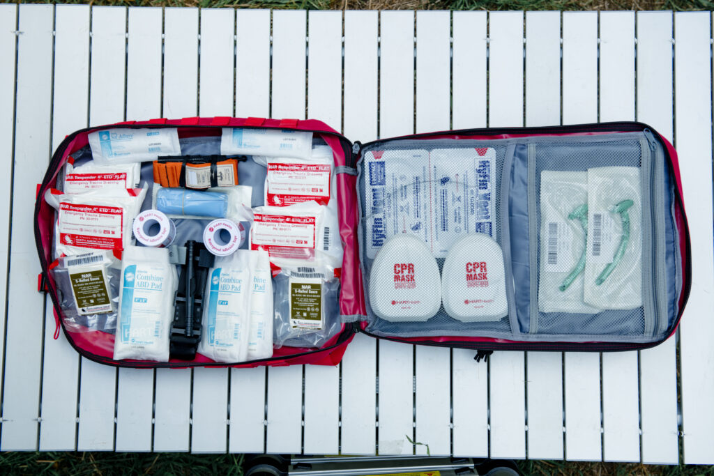 A first aid kit in a soft sided backpack laid out on a table