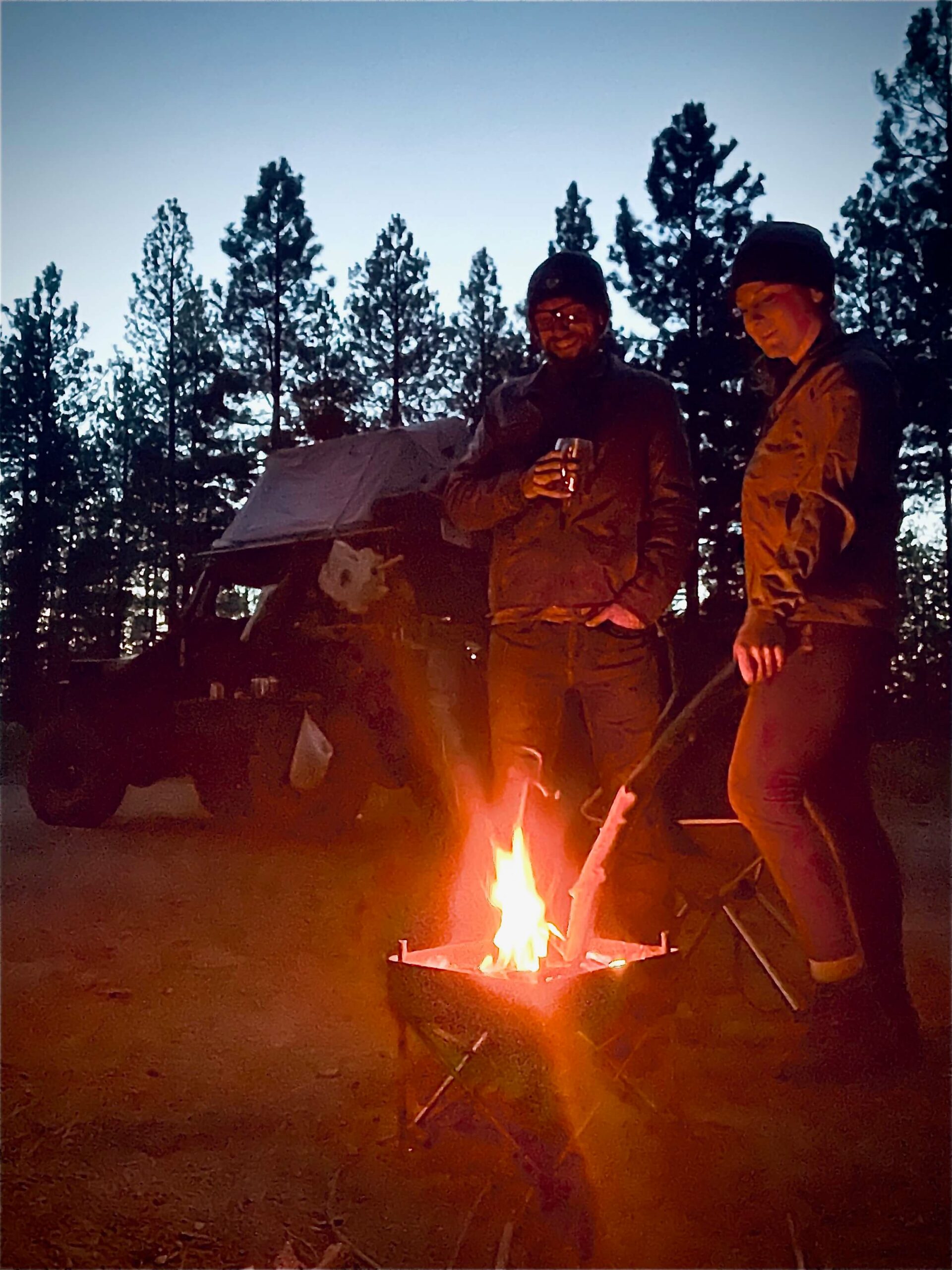 Blake and Chelsea stand in front of a campfire during an overlanding adventure.