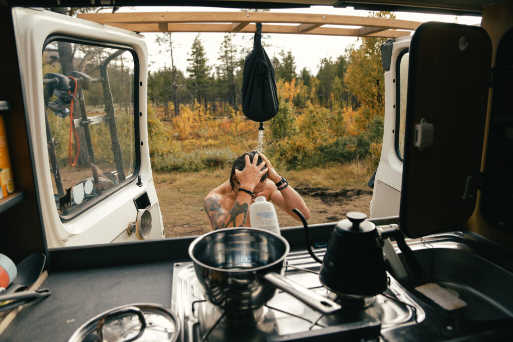 A man showers outside the window of his overland vehicle.