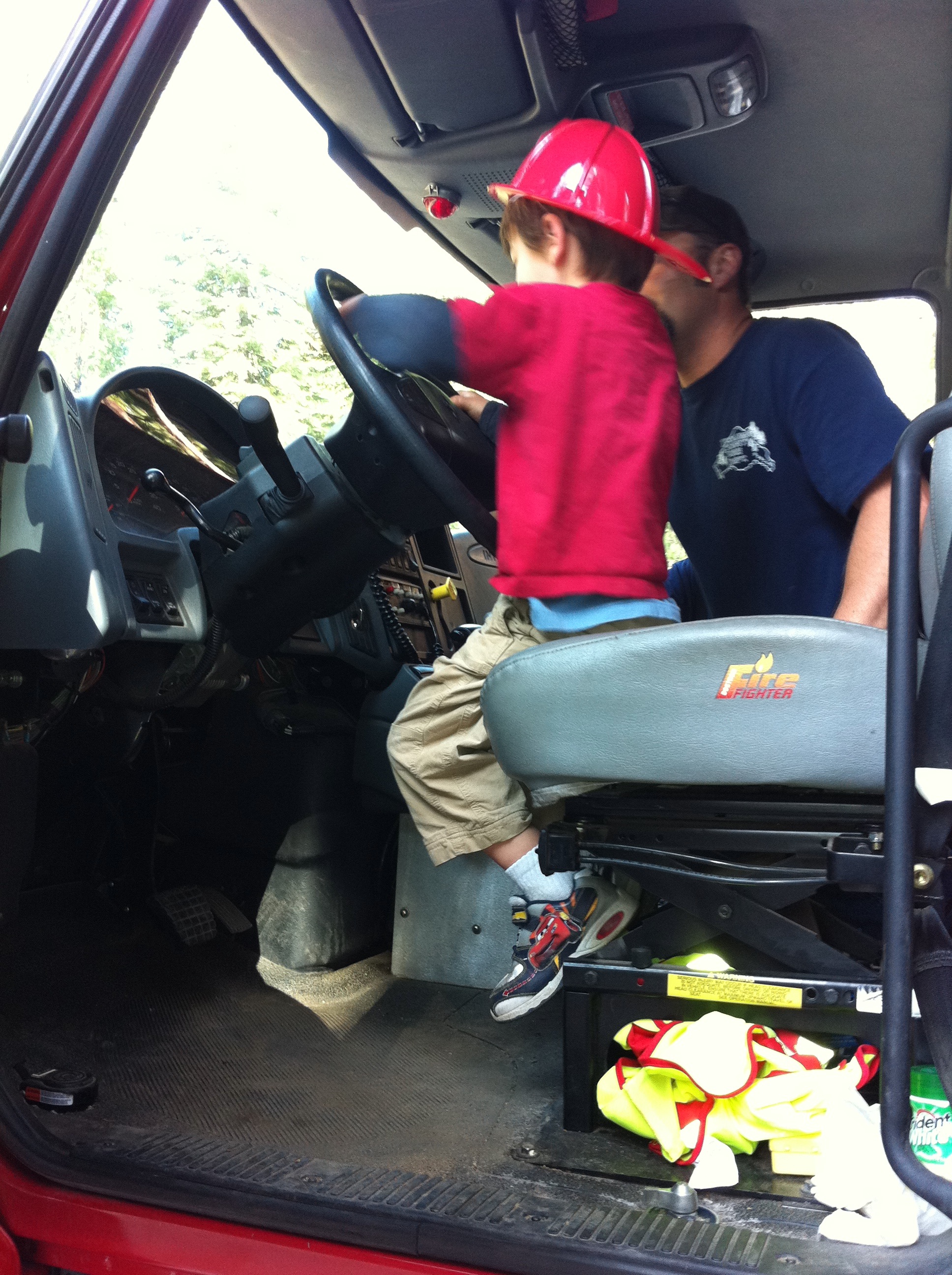 Little boy sits in the drivers seat of a fire truck