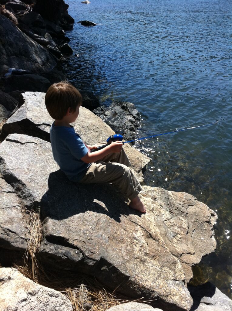 Young boy sits at edge of lake to fish.