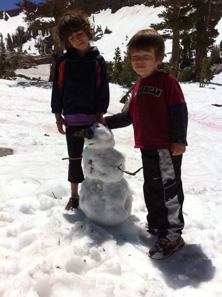 Two kids standing by their mini snowman